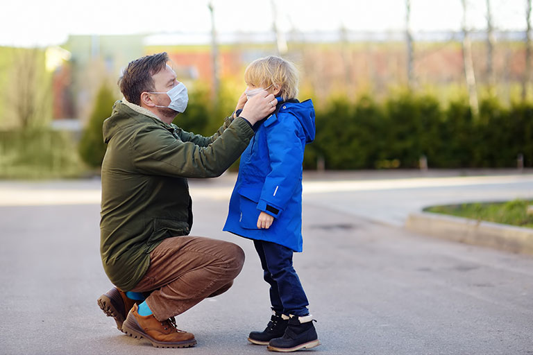 A parent placing a mask on their young child while in a public park.